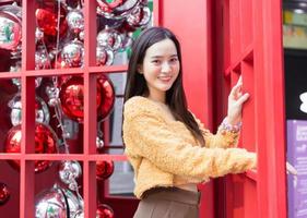 hermosa mujer asiática de pelo largo con una túnica amarilla sonríe feliz parada al lado de una cabina telefónica roja con el tema de celebrar la navidad y feliz año nuevo. foto