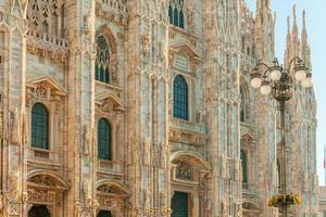 Famous church Milan Cathedral Duomo di Milano with Gothic spires and white marble statues. Top tourist attraction on piazza in Milan Lombardia Italy. Wide angle view of old Gothic architecture and art photo