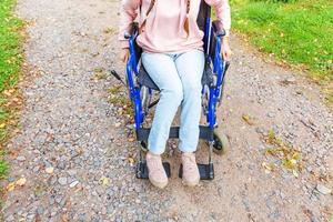 Legs feet handicap woman in wheelchair wheel on road in hospital park waiting for patient services. Unrecognizable paralyzed girl in invalid chair for disabled people outdoors. Rehabilitation concept. photo