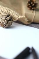 Holidays Gifts. Christmas and New Year Gift box wrapped in brown paper, pine cones and white paper and pens placed on the table, copy space. photo