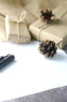 Holidays Gifts Christmas and New Year Gift box wrapped in brown paper, pine cones and white paper and pens placed on the table copy space. photo