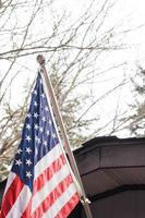 The American flag in front of the house against the backdrop of a leafless tree in winter. photo