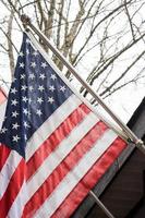 The American flag in front of the house against the backdrop of a leafless tree in winter. photo