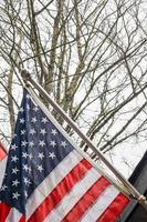 The American flag in front of the house against the backdrop of a leafless tree in winter. photo