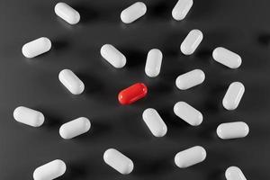 Red pill between white pills on black background 3d render. photo