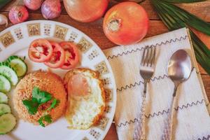 Fried Rice with Fried Egg Put on the wooden table and the tomatoes, cucumbers, garlic, shallots photo