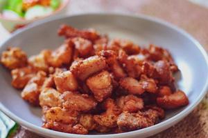 Fried Pork Belly with Fish Sauce and Sticky Rice Served on a white plate on a black wooden floor. photo