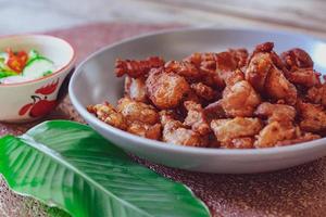 vientre de cerdo frito con salsa de pescado y arroz pegajoso servido en un plato blanco sobre un suelo de madera negra. foto