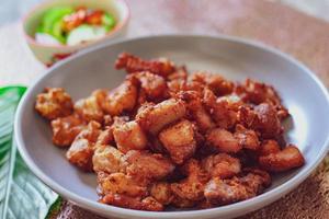 Fried Pork Belly with Fish Sauce and Sticky Rice Served on a white plate on a black wooden floor. photo