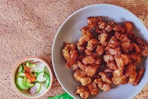 Fried Pork Belly with Fish Sauce and Sticky Rice Served on a white plate on a black wooden floor. photo