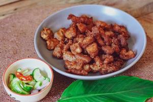 Fried Pork Belly with Fish Sauce and Sticky Rice Served on a white plate on a black wooden floor. photo