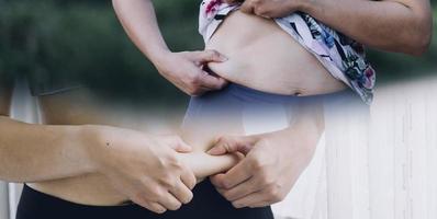 hermosa mujer gorda con cinta métrica usa su mano para exprimir el exceso de grasa que está aislado en un fondo blanco. ella quiere perder peso, el concepto de cirugía y descomponer grasa bajo el foto