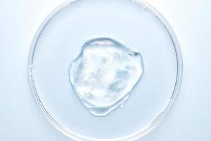 Petri dish with gel or cosmetic liquid on blue background closeup. Transparent container with gel with bubbles. Texture of the gel. Medicine and beauty concept. Medical glassware for laboratories photo