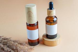 A mock-up of a brown cosmetics bottles with dispenser and white label and bottle with pipette on wooden podium for cosmetics photography on beige background photo