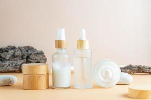 White frosted glass cosmetic bottles and jars with pamboo lids with tree bark, stones on beige background. Skin care routine set for aging skin photo