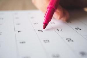 Hand with pen writing on calendar page closeup photo