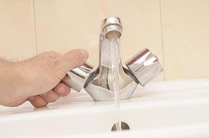 a man turns off a stainless steel faucet with water in the bathroom.Saving water in the house photo