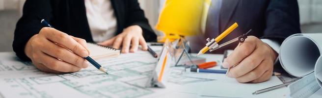 Two colleagues discussing data working and tablet, laptop with on on architectural project at construction site at desk in office photo