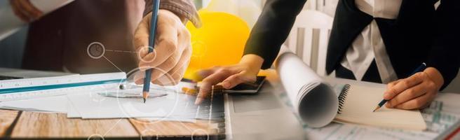 Two colleagues discussing data working and tablet, laptop with on on architectural project at construction site at desk in office photo