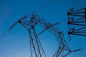 silhouette electric towers supporting copper cables to transport electric energy photo