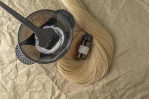 un mechón de cabello rubio junto al cepillo para teñir y teñir el cabello y suero o aceite para el cabello foto