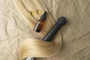 A hair treatment essential oil for smoothing hair and a hair curling styler lying on a brown craft paper background photo