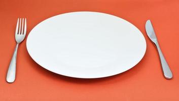 white porcelain plate with fork and knife on red photo