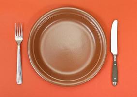 top view of ceramic plate, fork, knife on red photo