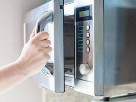 la mano abre el horno de microondas para cocinar alimentos foto