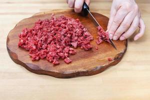 mujer corta finamente la carne en la tabla de cortar foto