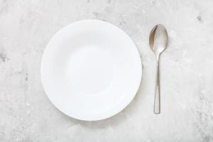 top view of white deep plate and spoon on concrete photo