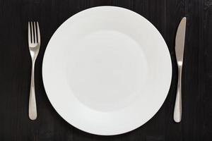 top view of white plate with knife, spoon on dark photo