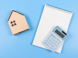 flat layout of wooden house model , opened blank page notebook and  blue calculator  on blue background with copy space.  home purchase concept. photo