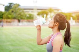 mujer joven relajándose y bebiendo agua después del entrenamiento físico en el estadio de fútbol por la mañana. foto