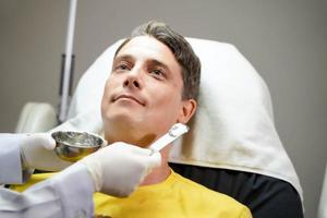 Closeup handsome man receiving skin gel to prepare the color light therapy to stimulate facial health. photo