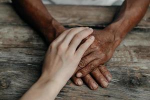 Hands of the old man and a woman hand on the wood table in sun light photo