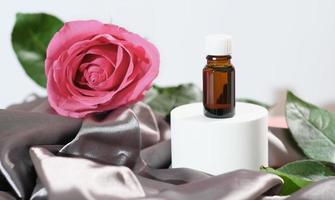 rose petals oil. essential oil for face care and skin moisturizing. a bottle of aroma oil and fresh pink rose on silk sheet. photo