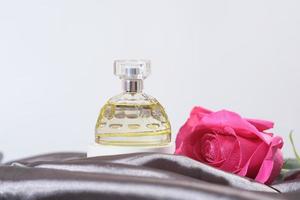 female perfume bottle on a grey silk background with pink fresh rose bud. gift for a woman, fragrances for women, perfumery shop. photo