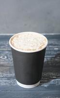 café para llevar en vaso de papel. café con espuma de leche, café con leche o capuchino sobre mesa de madera. bebidas para llevar en vaso sin plástico. foto