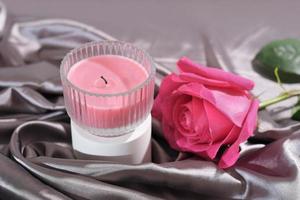 pink rose and soy wax candle on silk satin draped bedding sheet. romantic date, celebration or proposal evening. photo