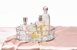 various bottles of perfume on a trendy mirror tray. pink silk satin fabric background. female perfume set. fragrances for woman