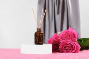 Aromatic reed air freshener and roses. amber glass bottle with sticks and silk drapery. Home scents, aromatherapy concept. photo