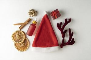 A face serum or essential oil for Christmas holidays in a red dropper bottle lying on a white background with golden bows, cinnamon and dried oranges around photo