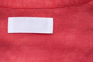 White blank clothing tag label on red linen shirt fabric texture background photo