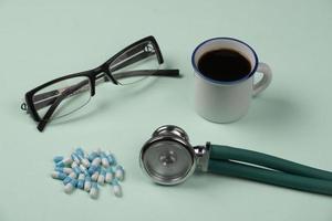 objeto médico sobre fondo verde claro, con gafas, pastillas, estetoscopio y taza de café foto