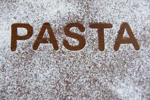 wooden background with sprinkled flour and the word pasta written photo