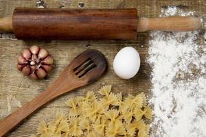 kitchen supplies to prepare pasta on rustic board with egg and garlic photo