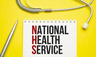 NATIONAL HEALTH SERVICE is written in a notebook with stethoscope on yellow background