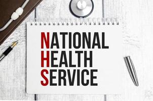 NATIONAL HEALTH SERVICE is written in a notebook with stethoscope photo