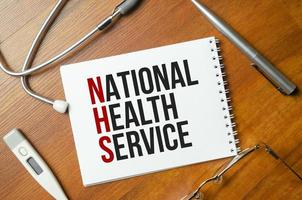 NATIONAL HEALTH SERVICE is written in a notebook with stethoscope photo
